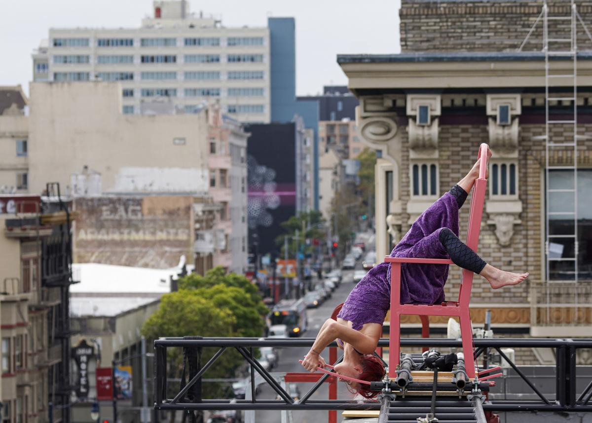 dancer in purple costume hanging upside down in a pink rocking chair suspended 60 feet in the air 