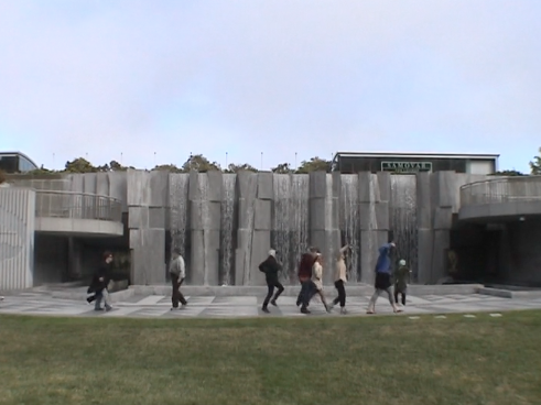 A handful of dancers traversing the concrete from left to right in front of the magnificent waterfall at Yerba Buena Gardens.